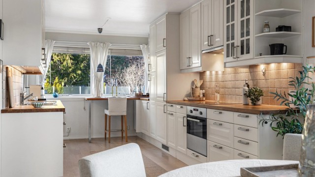 Kjøkken med innredning fra rundt 2010. Profilerte fronter. Benkeplate av tre. Nedfelt kjøkkenvask med armatur. Benkeskapsbelysning og stikkontakter over kjøkkenbenk.