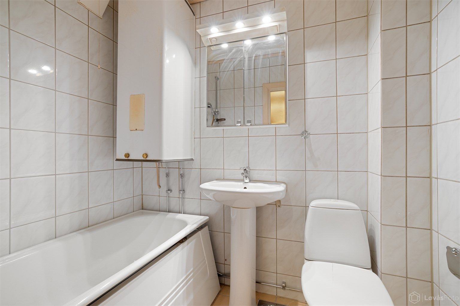 Badet har flislagte overflater med gulvvarme, badekar, servant og speilskap med belysning.