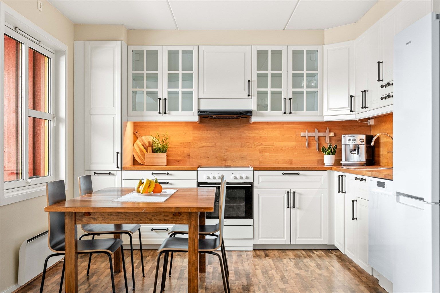 Kjøkkenet har en praktisk hjørneløsning med hvite, profilerte fronter og benkeplate i heltre.