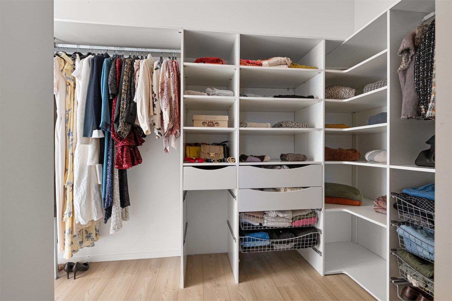 Walk-in closet innredet med åpne garderobeløsninger, skuffer og hyller.