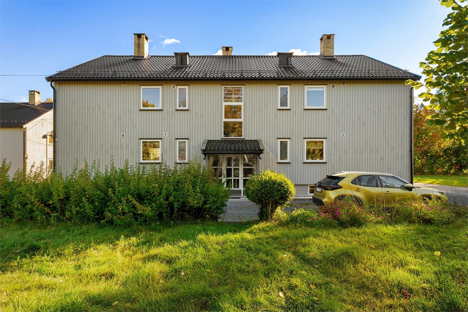 Leilighetsbygget fra 1958 er kledd med stående trekledning og omgitt av plenarealer.