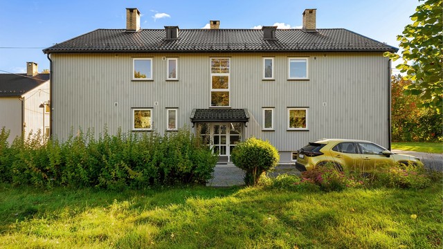 Leilighetsbygget fra 1958 er kledd med stående trekledning og omgitt av plenarealer.