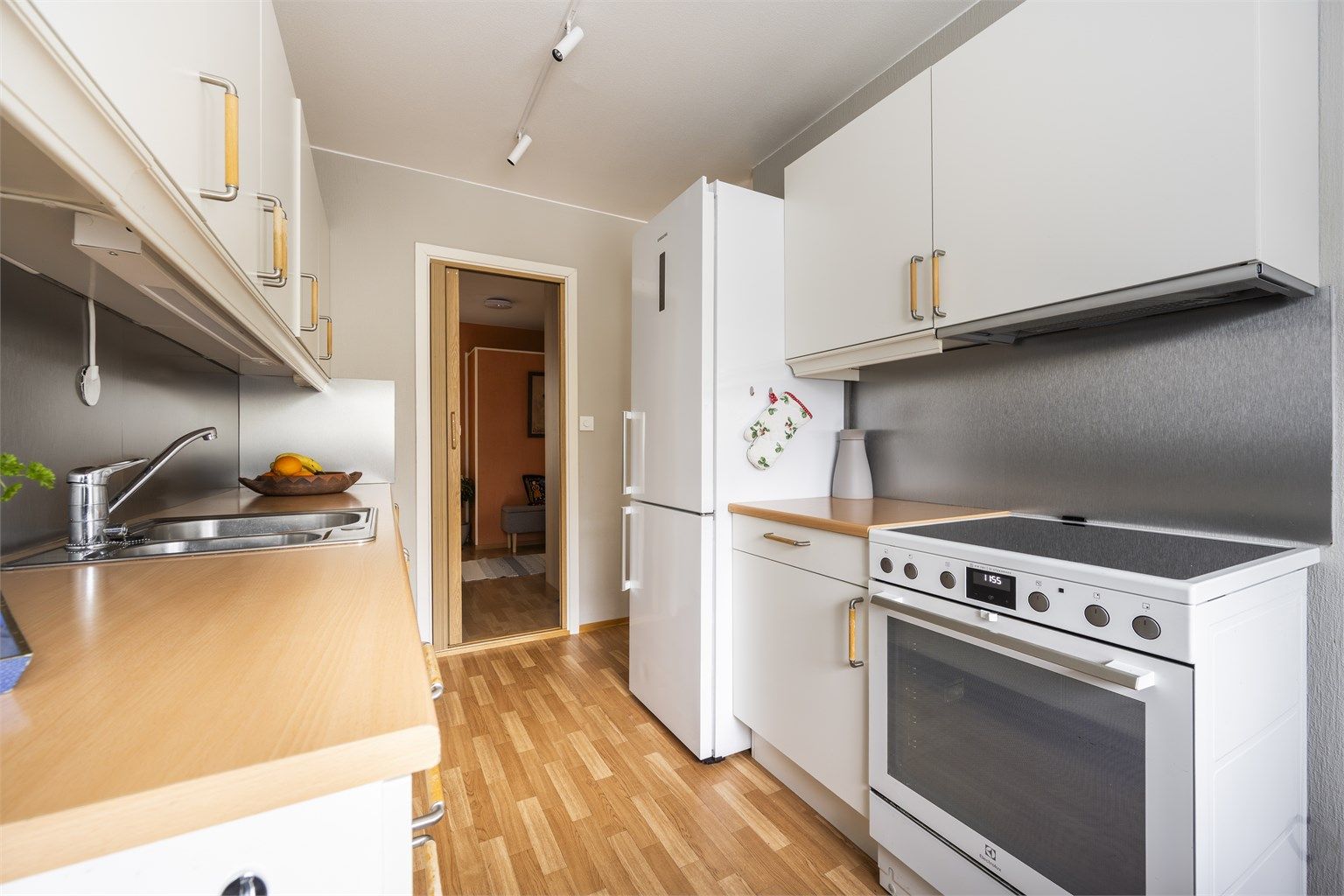 Kjøkkeninnredning med glatte fronter og benkeplate med nedfelt vask. Frittstående kjøleskap, komfyr og oppvaskmaskin medfølger. Kullfilterventilator over kokeplass
