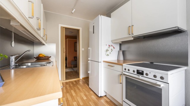 Kjøkkeninnredning med glatte fronter og benkeplate med nedfelt vask. Frittstående kjøleskap, komfyr og oppvaskmaskin medfølger. Kullfilterventilator over kokeplass