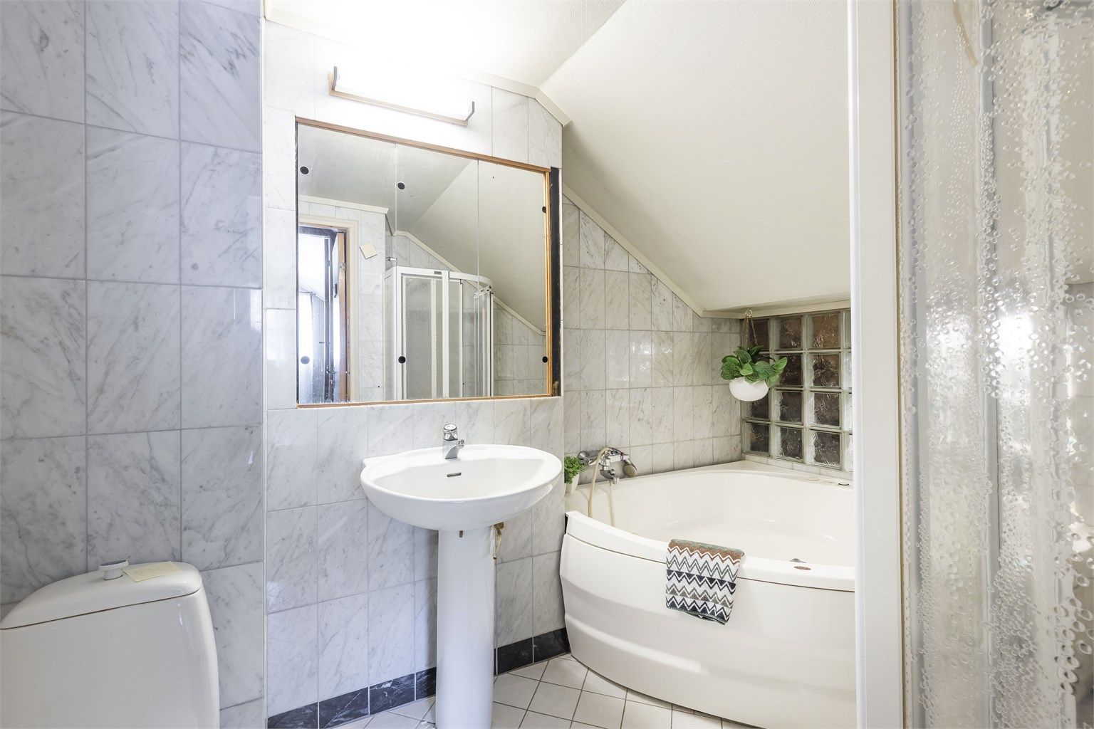 Badet inneholder dusjnisje, badekar, servant og toalett