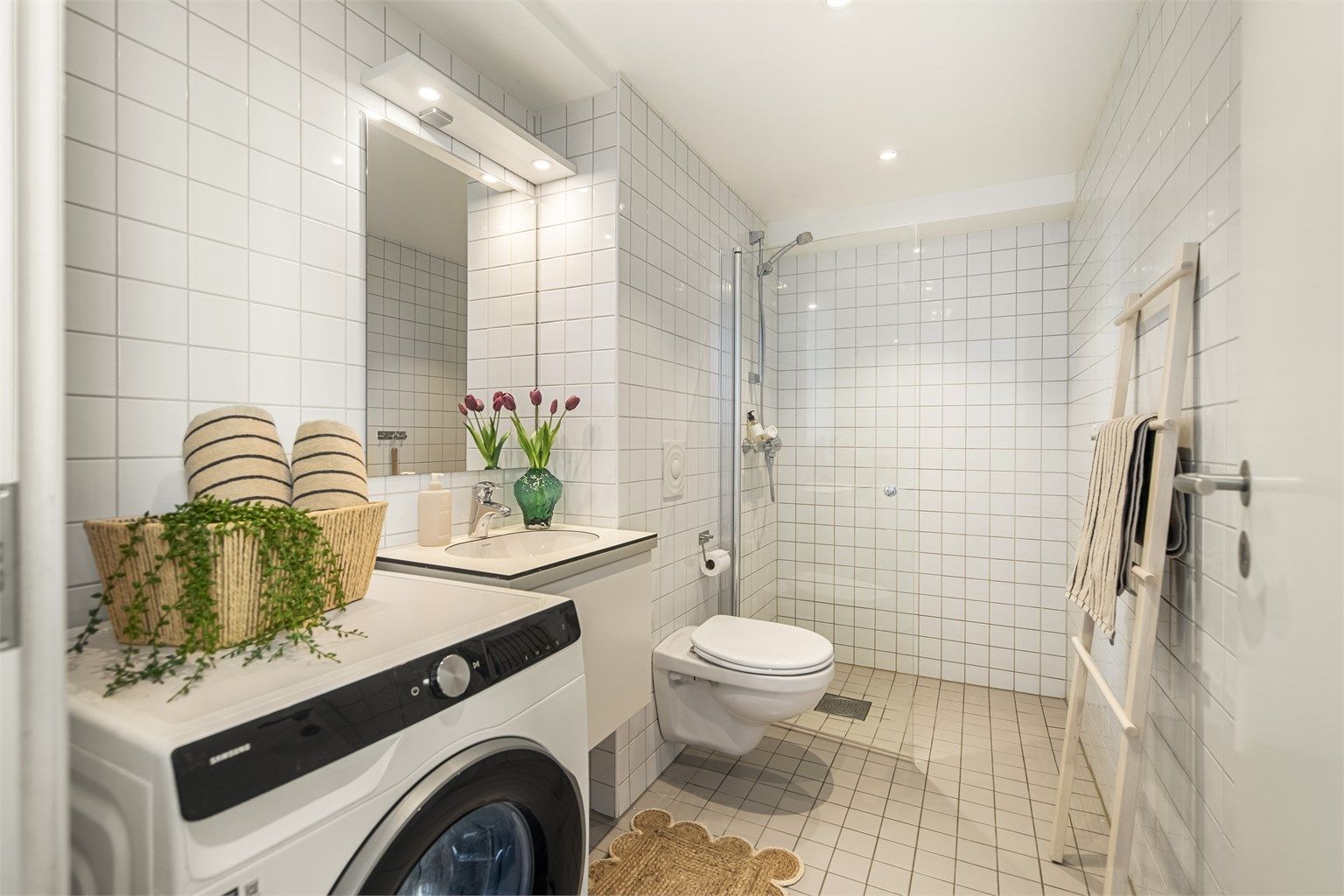 Badet har flislagt gulv med gulvvarme og flislagte vegger. Himlingen har malt, slett overflate med innfelte downlights. 