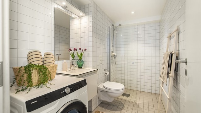 Badet har flislagt gulv med gulvvarme og flislagte vegger. Himlingen har malt, slett overflate med innfelte downlights.