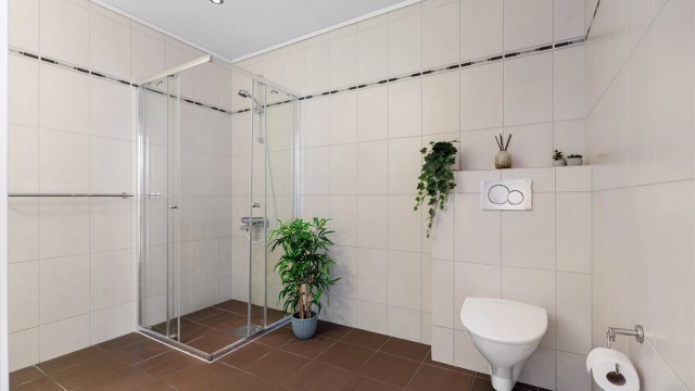 Videre er badet innredet med dusjhjørne og vegghengt toalett.