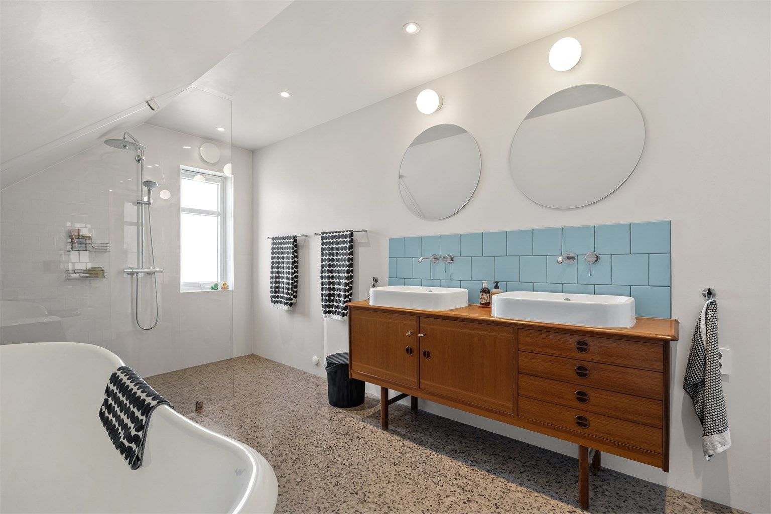 Et romslig og lekkert bad med både dusjnisje og et frittstående badekar av støpejern. Det er gulvvarme og innfelte downlights i taket.