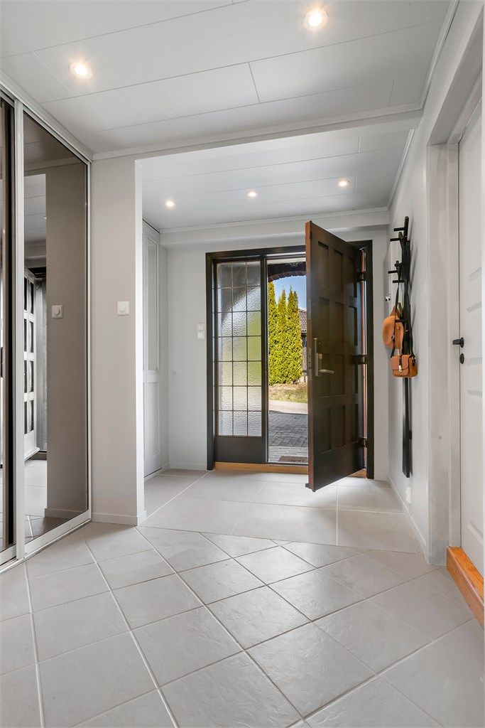 En romslig entré ønsker deg velkommen inn. Her er det flislagt gulv og skyvedørsgarderobe.