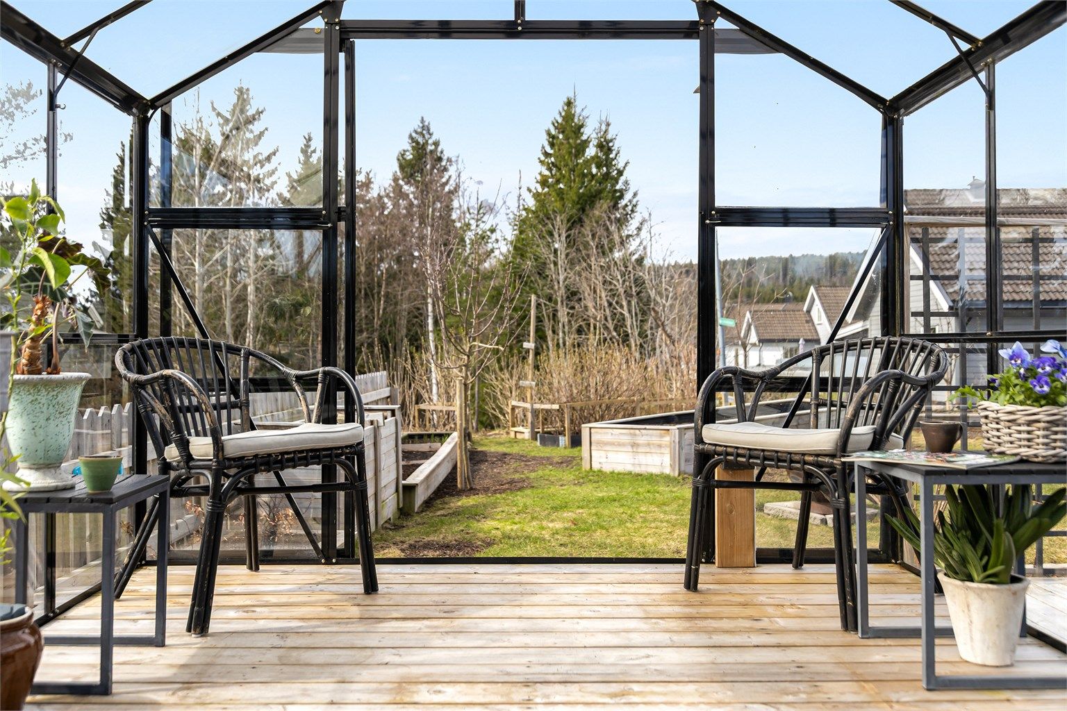 Fra drivhuset ser man ut over hagen med plenarealer og plantekasser.