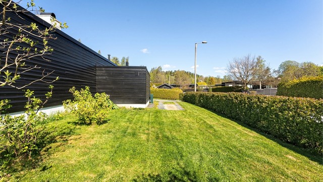 Tomten er opparbeidet med plenarealer, bærbusker og hekk som skjermer for veien.