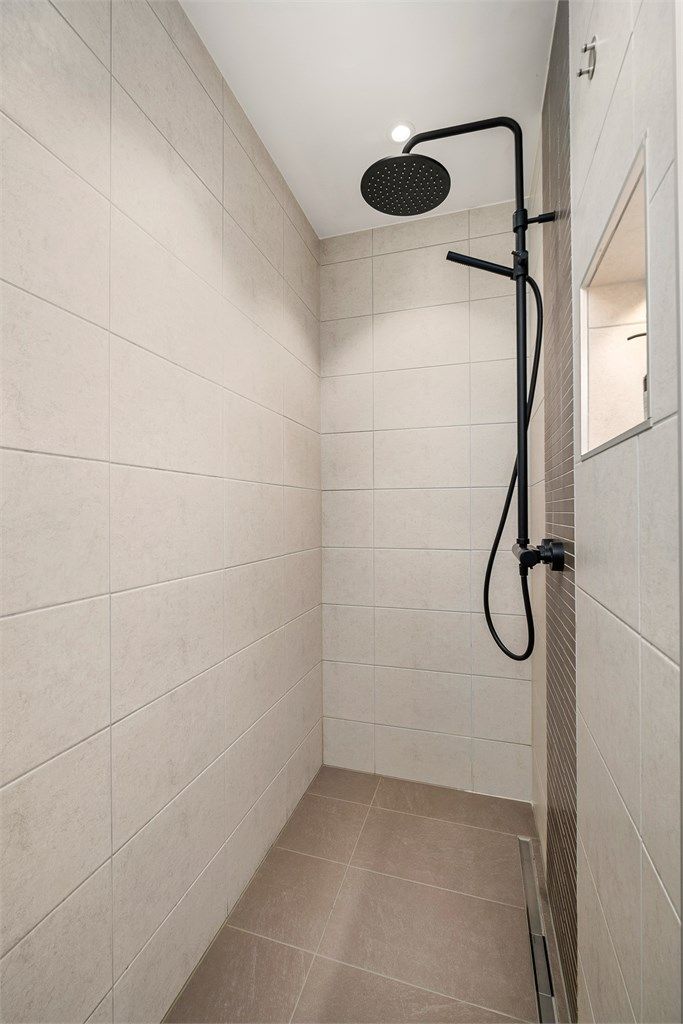 Badet har en romslig dusjsone med både takdusj og hånddusj. Badet er videre innredet med badekar, vegghengt toalett og praktiske oppbevaringsløsninger i en gjennomført utførelse.