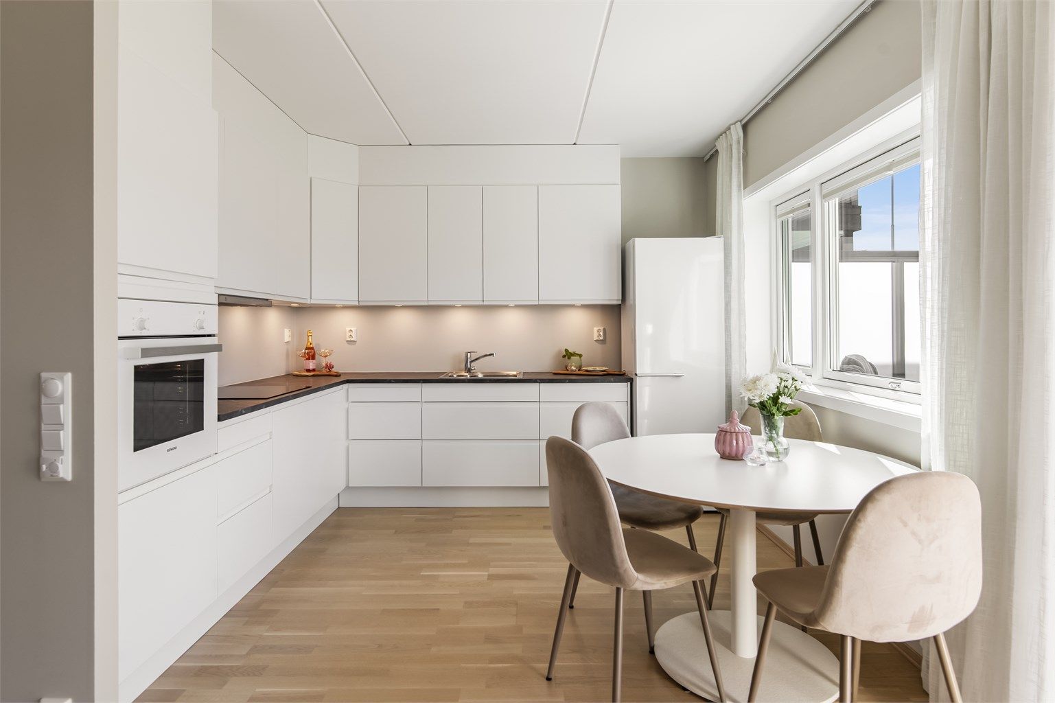 Kjøkkeninnredning fra Sigdal med slette fronter og laminert benkeplate, utstyrt med integrert stekeovn, induksjonstopp og oppvaskmaskin.