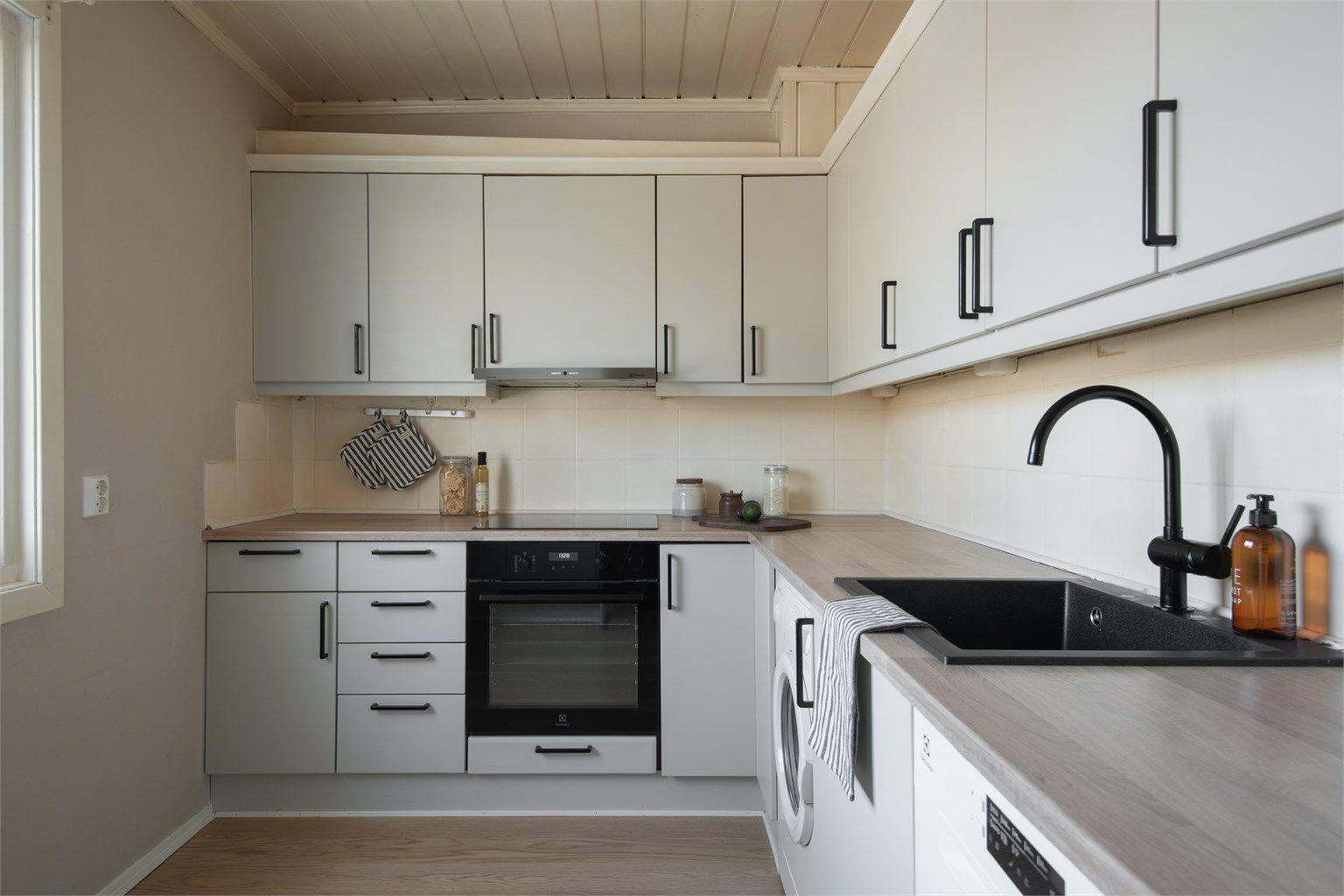 Praktisk kjøkken med glatte fronter, integrerte hvitevarer og opplegg for vaskemaskin.