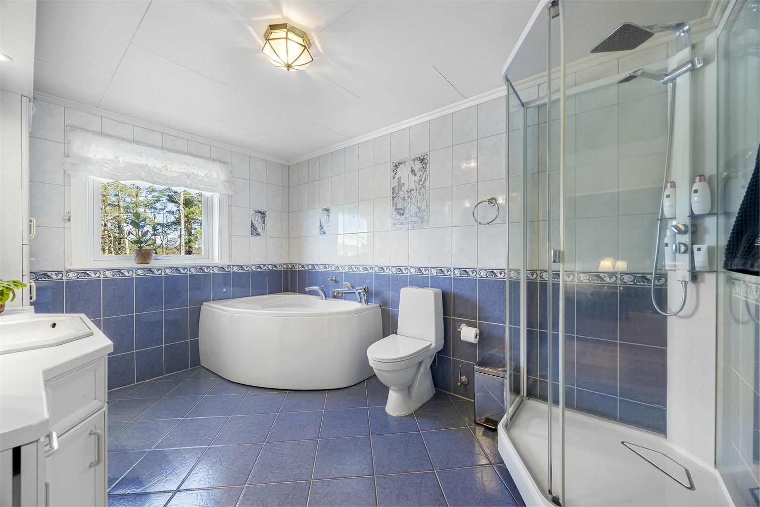 Badet er utstyrt med både badekar og dusjkabinett, samt toalett og servant med innredning.