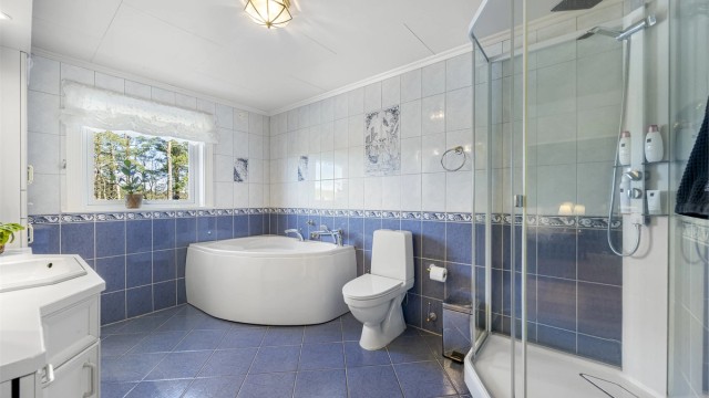 Badet er utstyrt med både badekar og dusjkabinett, samt toalett og servant med innredning.