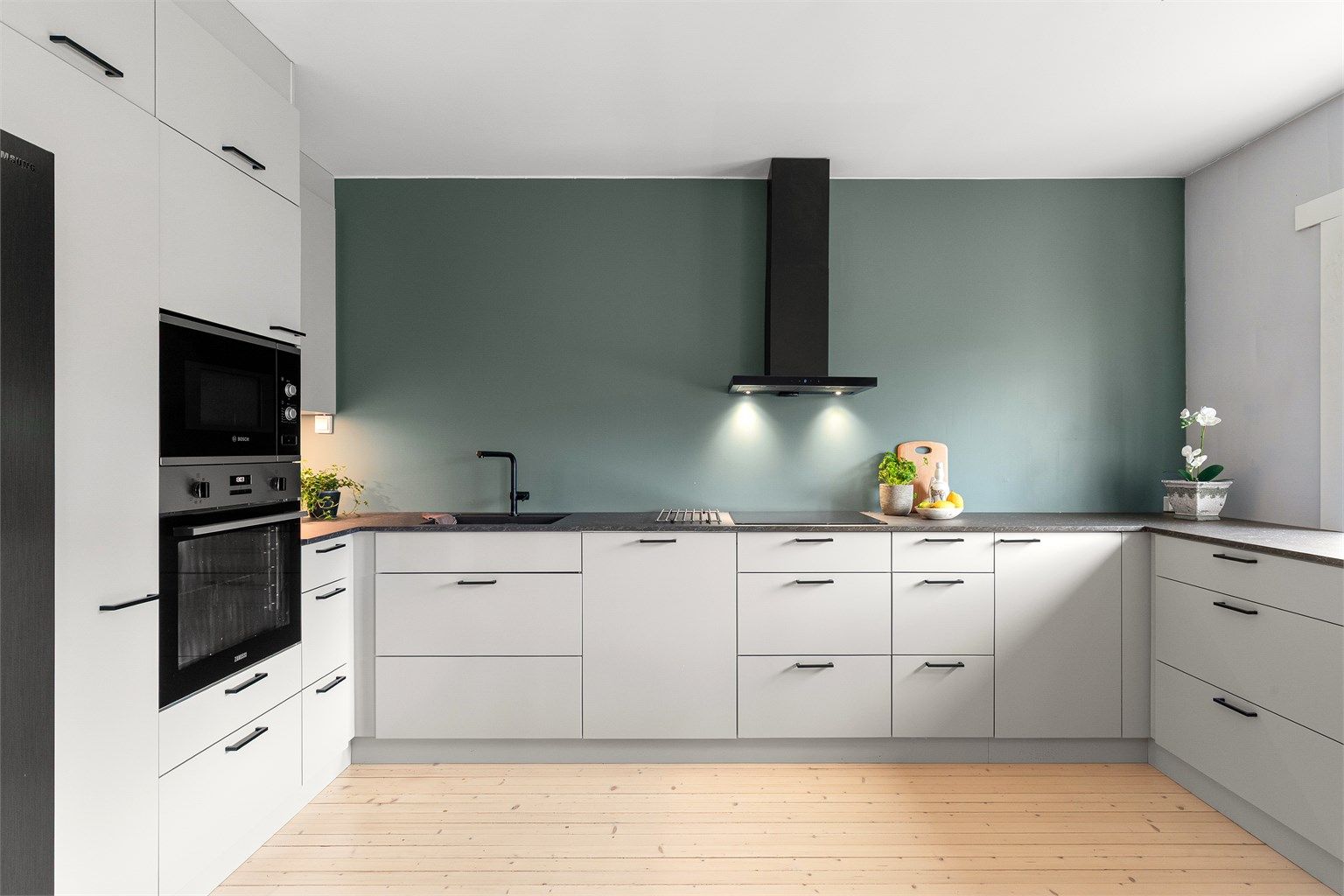 Moderne og tidløst kjøkken fra Kvik med en praktisk og stilren benkeplate av laminat, induksjonstopp, fritthengende ventilator med kullfilter og overskapsbelysning. 
