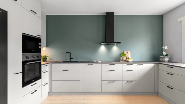 Moderne og tidløst kjøkken fra Kvik med en praktisk og stilren benkeplate av laminat, induksjonstopp, fritthengende ventilator med kullfilter og overskapsbelysning.
