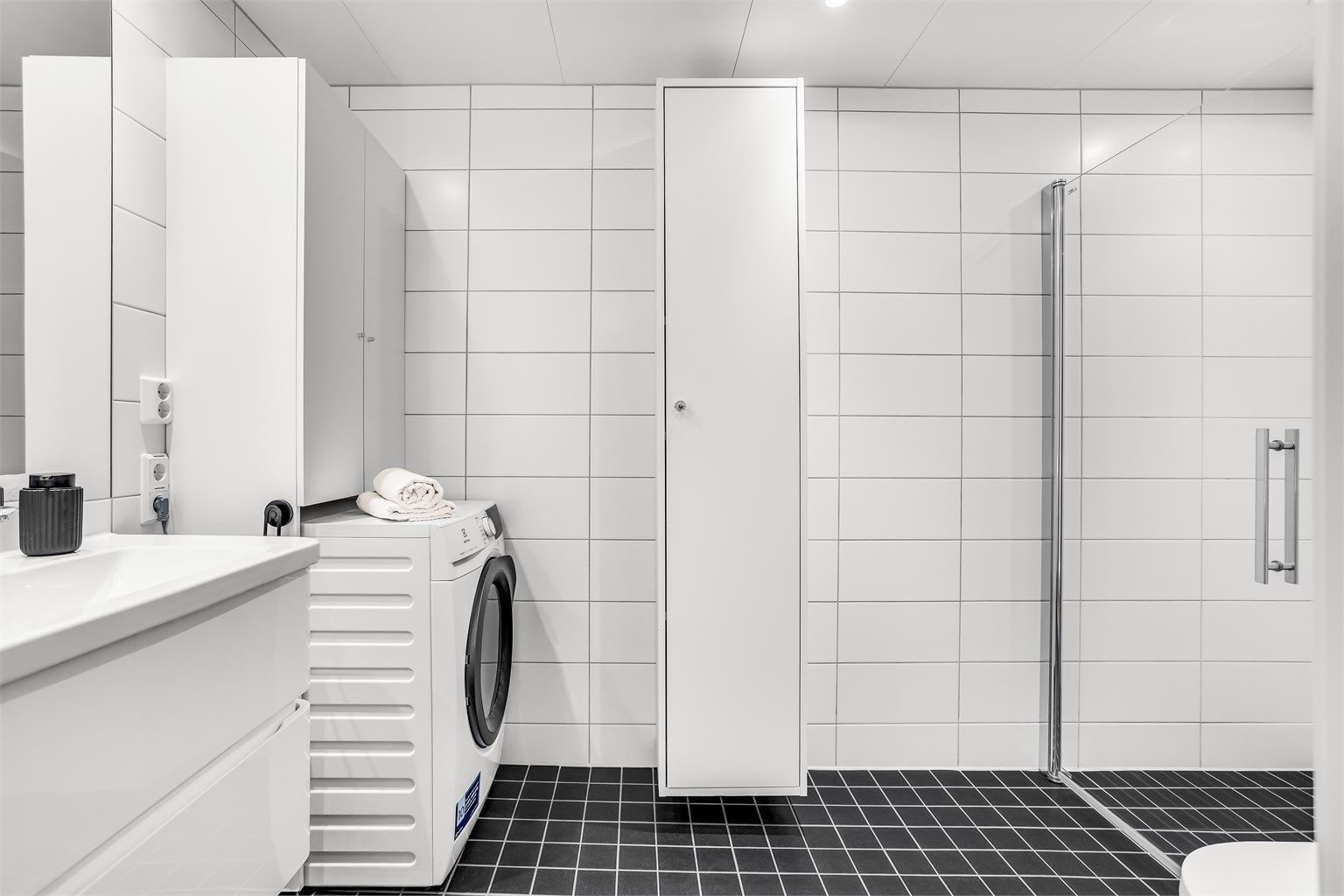 Flislagt bad med varmekabler i gulvet, innfellbare dusjvegger og opplegg for vaskemaskin.
