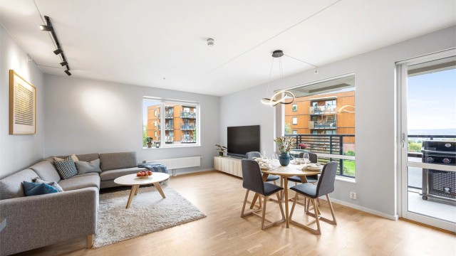 Lyst oppholdsrom med store vindusflater og innvendig solskjerming.