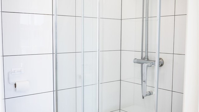 Badet har dusjhjørne med skyvedørsramme og veggmontert regnfallsdusj.