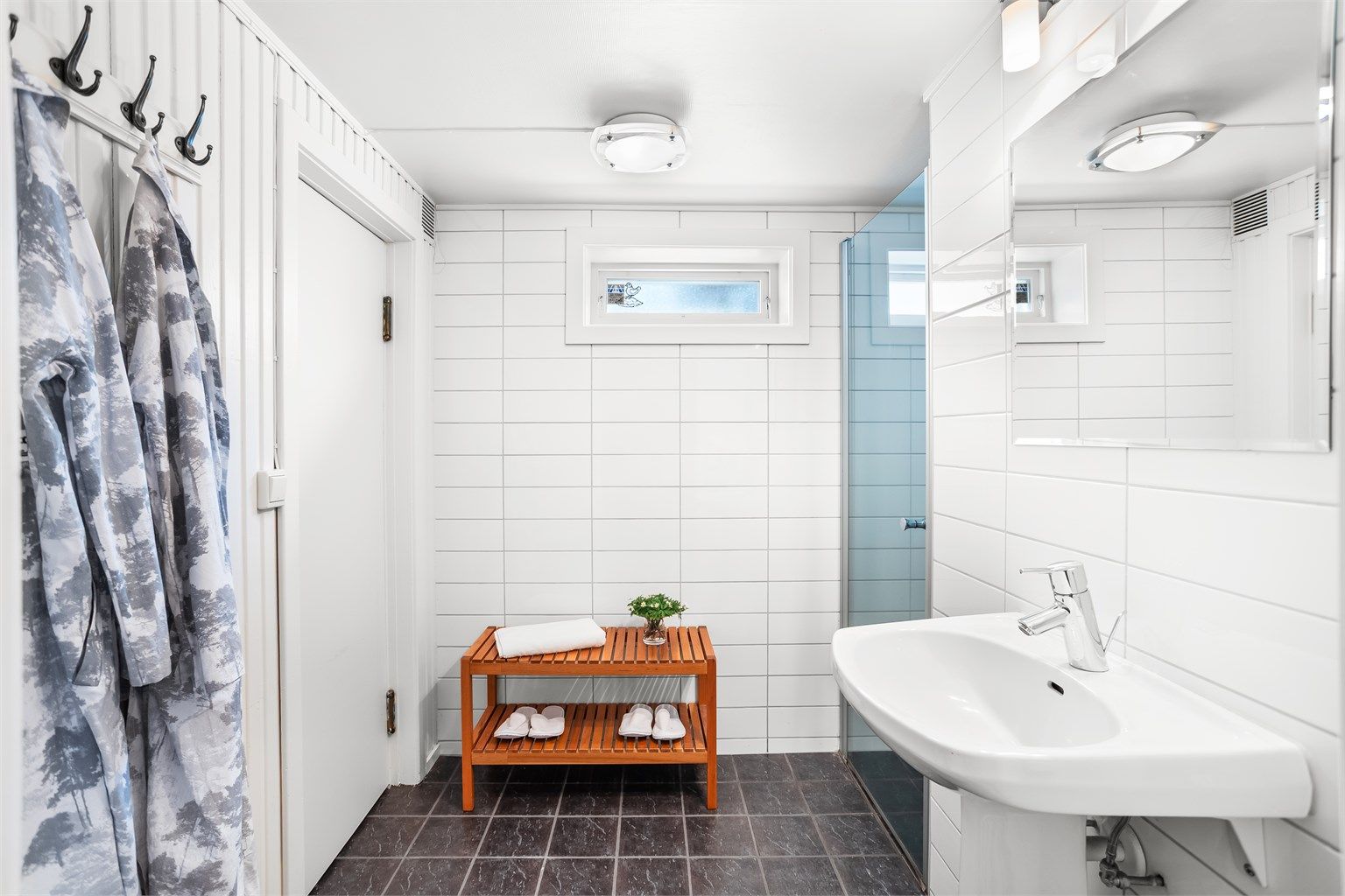 Badet i kjelleren består videre av flislagt gulv med varme, vegghengt servant, speil med overlys og en dusjnisje, i tillegg til inngang til badstuen her. 