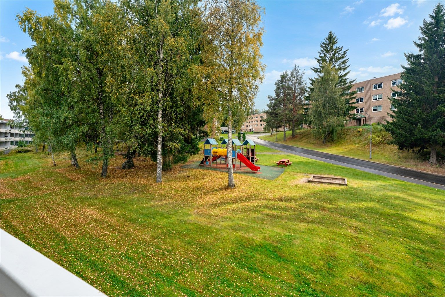 Utsikt fra balkongen over ett av borettslagets grønne fellesområde og lekeplass.