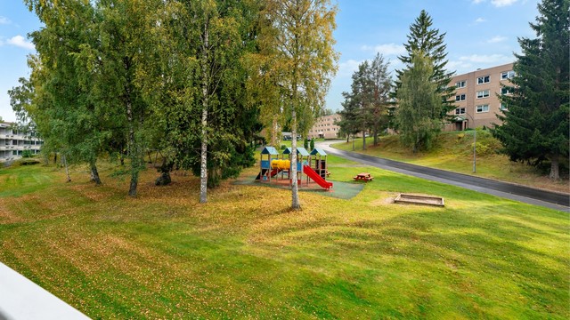Utsikt fra balkongen over ett av borettslagets grønne fellesområde og lekeplass.