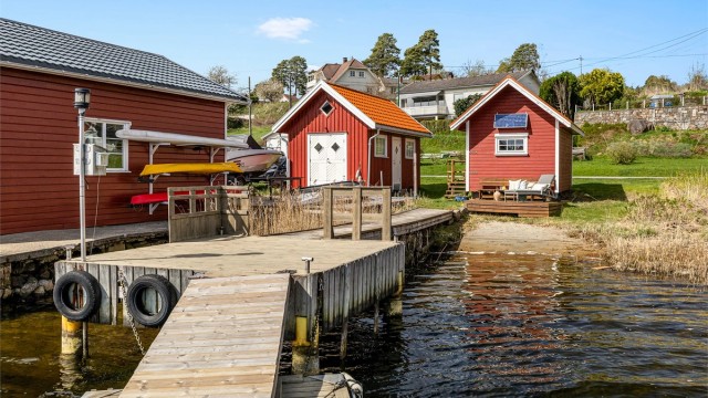 Nede ved sjøen ligger sjøboder og brygger på rekke og rad. Den til høyre i bildet hører til eiendommen, det samme gjør brygga.