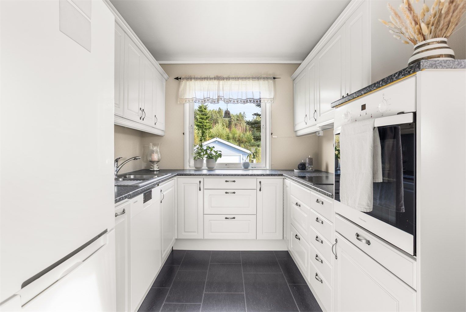 Kjøkken med hvite under og overskap. Det er blandt annet inkludert hvitevarer som oppvaskmaskin, komfyrplate og stekeovn