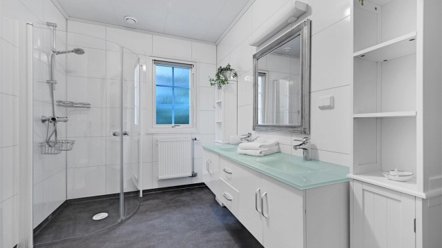 Badet i første etasje har elektrisk gulvvarme og radiator, baderomsplater på veggene og dusjhjørne med innfellbare dører.
