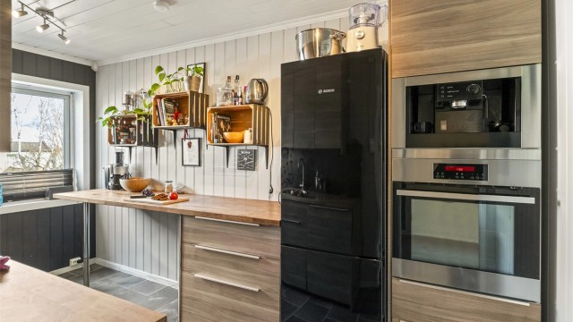 Pent kjøkken utstyrt med høyskap med b.la. stekeovn og kaffemaskin.