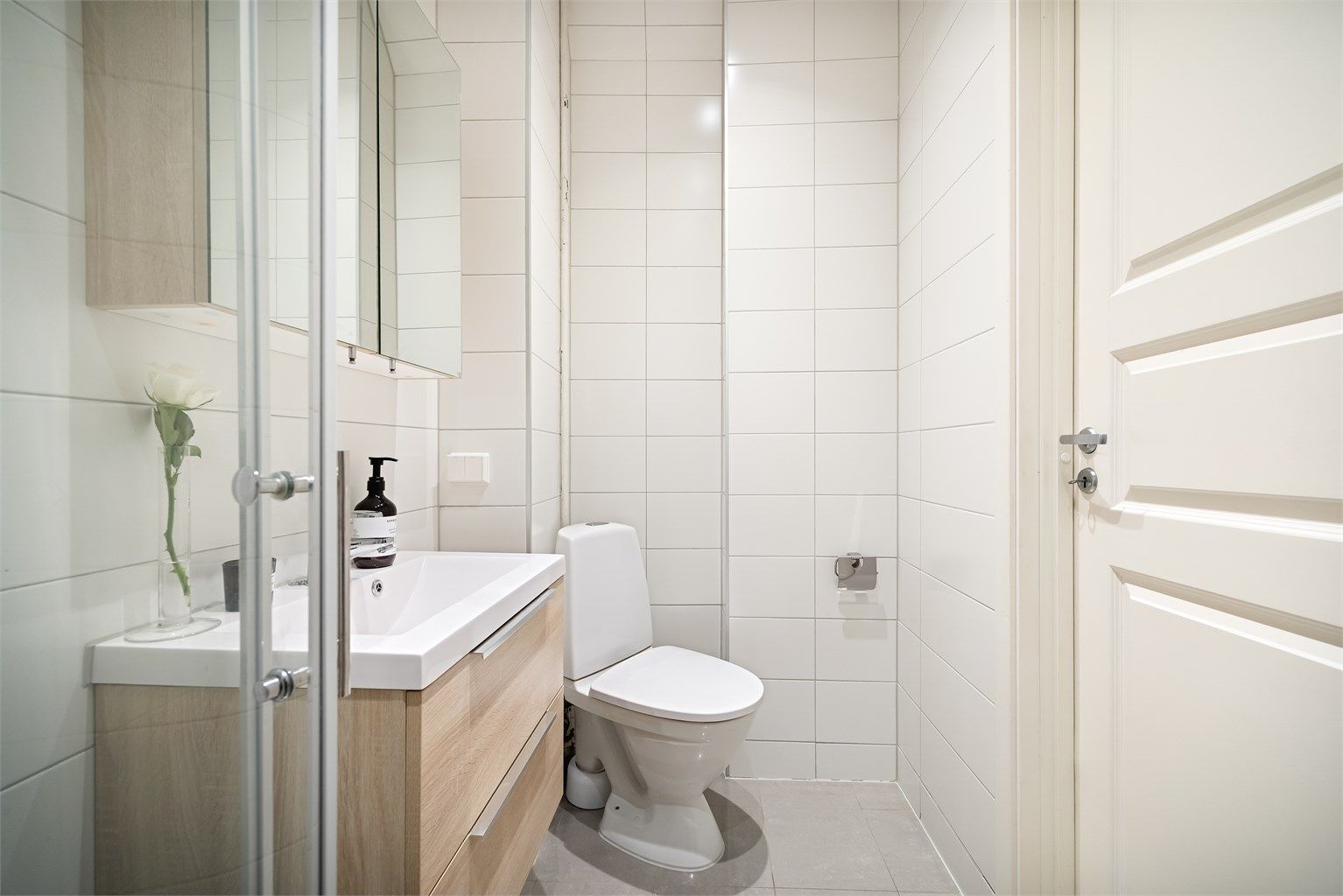Badet inneholder gulvmontert toalett, vegghengt servantinnredning med skuffer og ovenpåliggende vask, samt dusjhjørne.
