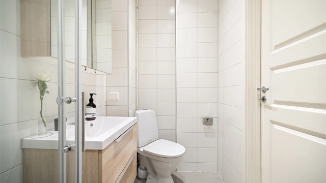 Badet inneholder gulvmontert toalett, vegghengt servantinnredning med skuffer og ovenpåliggende vask, samt dusjhjørne.