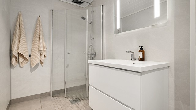 Badet er utstyrt med pen vegghengt servantinnredning, dusjhjørne med glassdører og vegghengt toalett.