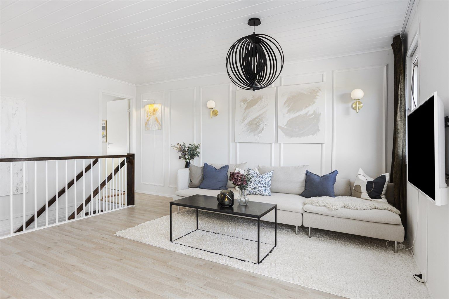 Lys og innbydende stue med laminatgulv og hvitmalte vegger med dekorativ brystpanel. 