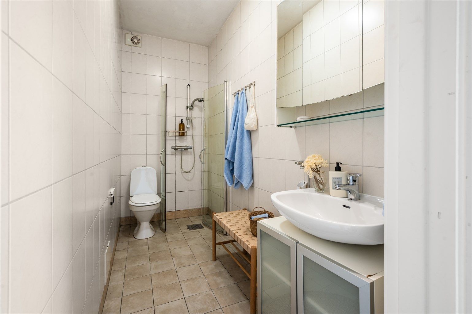 Badet er innredet med flislagte overflater og dusjhjørne med svingbare glassdører.
