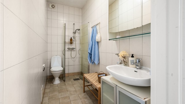 Badet er innredet med flislagte overflater og dusjhjørne med svingbare glassdører.