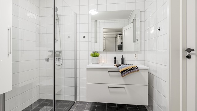 Hvit baderomsinnreding med glatte fronter og skuffer med ovenpåliggende servant med ett-greps armatur. Speil med sidelys over servant
