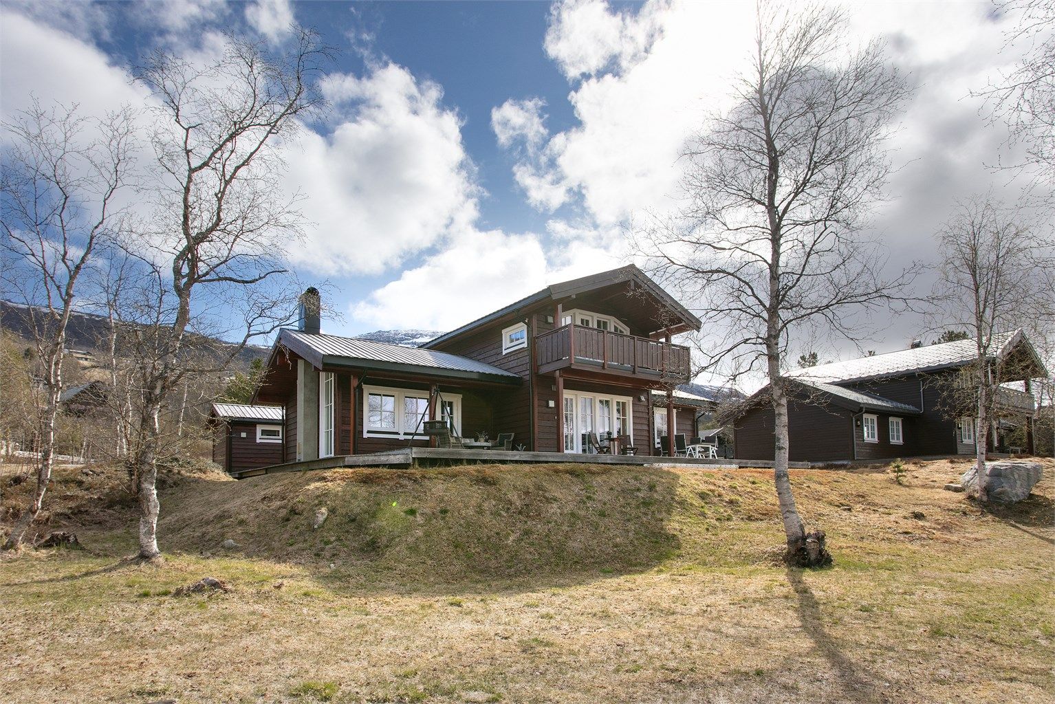 Hytta ligger fint til i terrenget, omgitt av bjørkeskog og med utsikt mot fjellene.