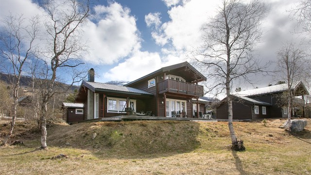 Hytta ligger fint til i terrenget, omgitt av bjørkeskog og med utsikt mot fjellene.