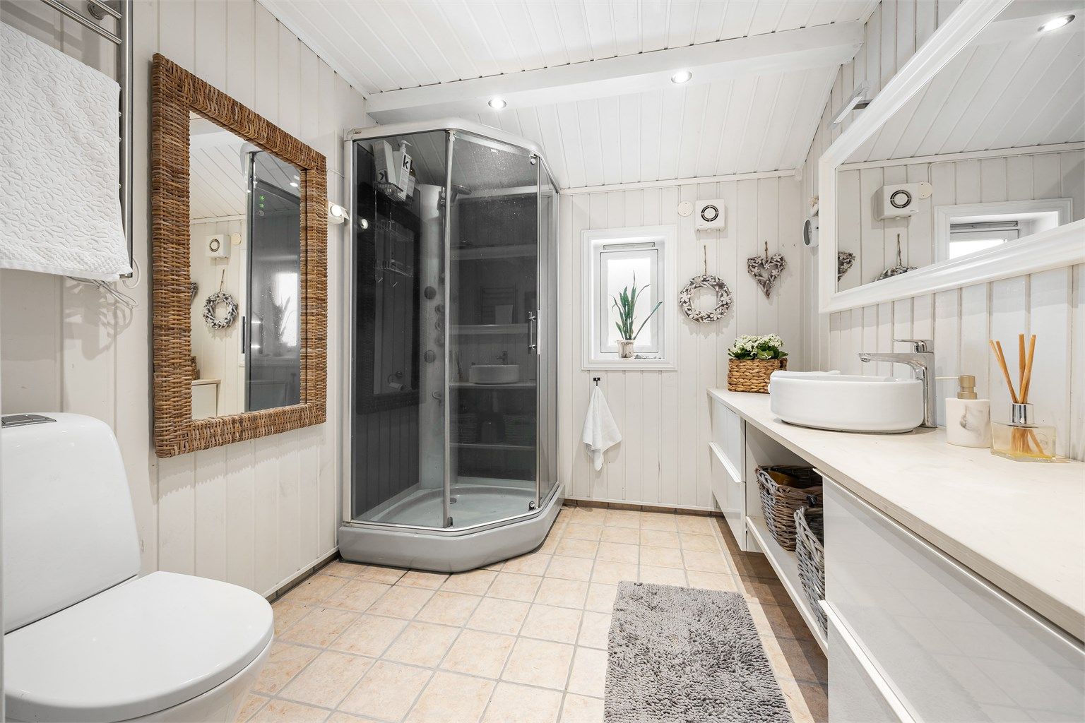 Badet i 2. etasje har flislagt gulv med varmekabler, dusjkabinett og en bred servantinnredning.