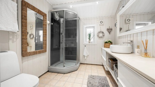 Badet i 2. etasje har flislagt gulv med varmekabler, dusjkabinett og en bred servantinnredning.