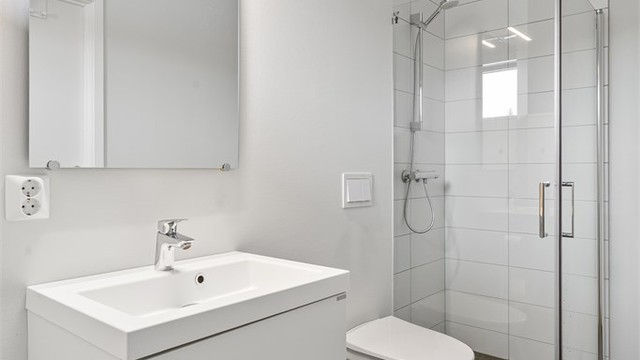 Dusjhjørne med innfellbare glassdører og vegghengt toalett for enkelt renhold.