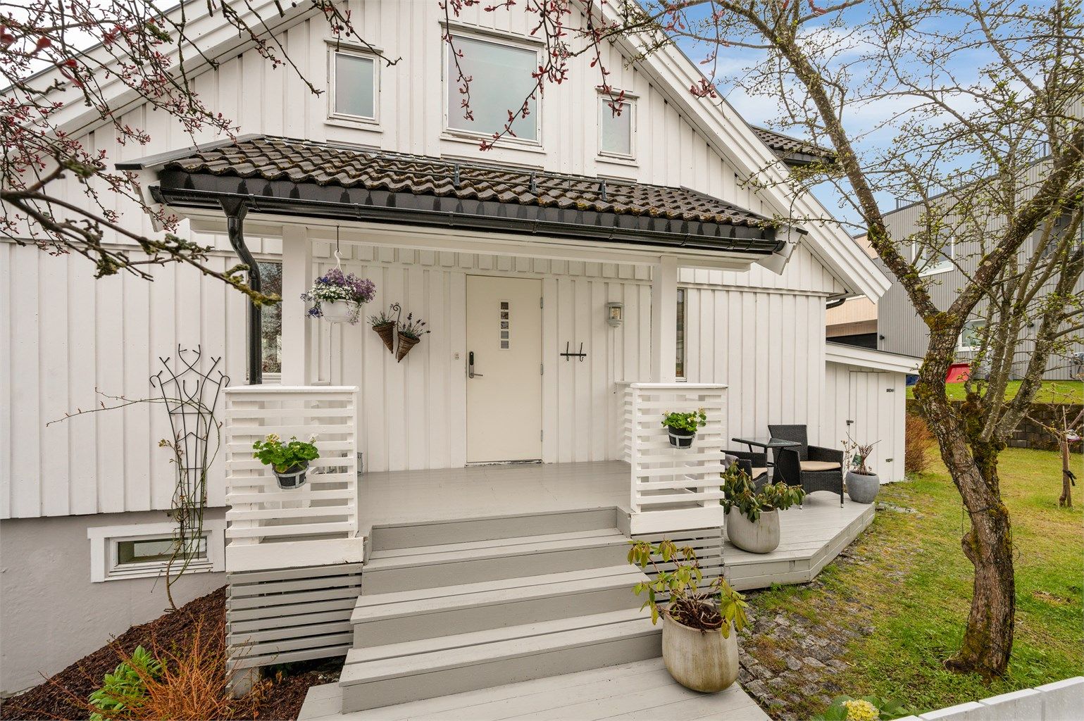 Pent, innbydende inngangsparti, omrammet av vakre trær med blomster.