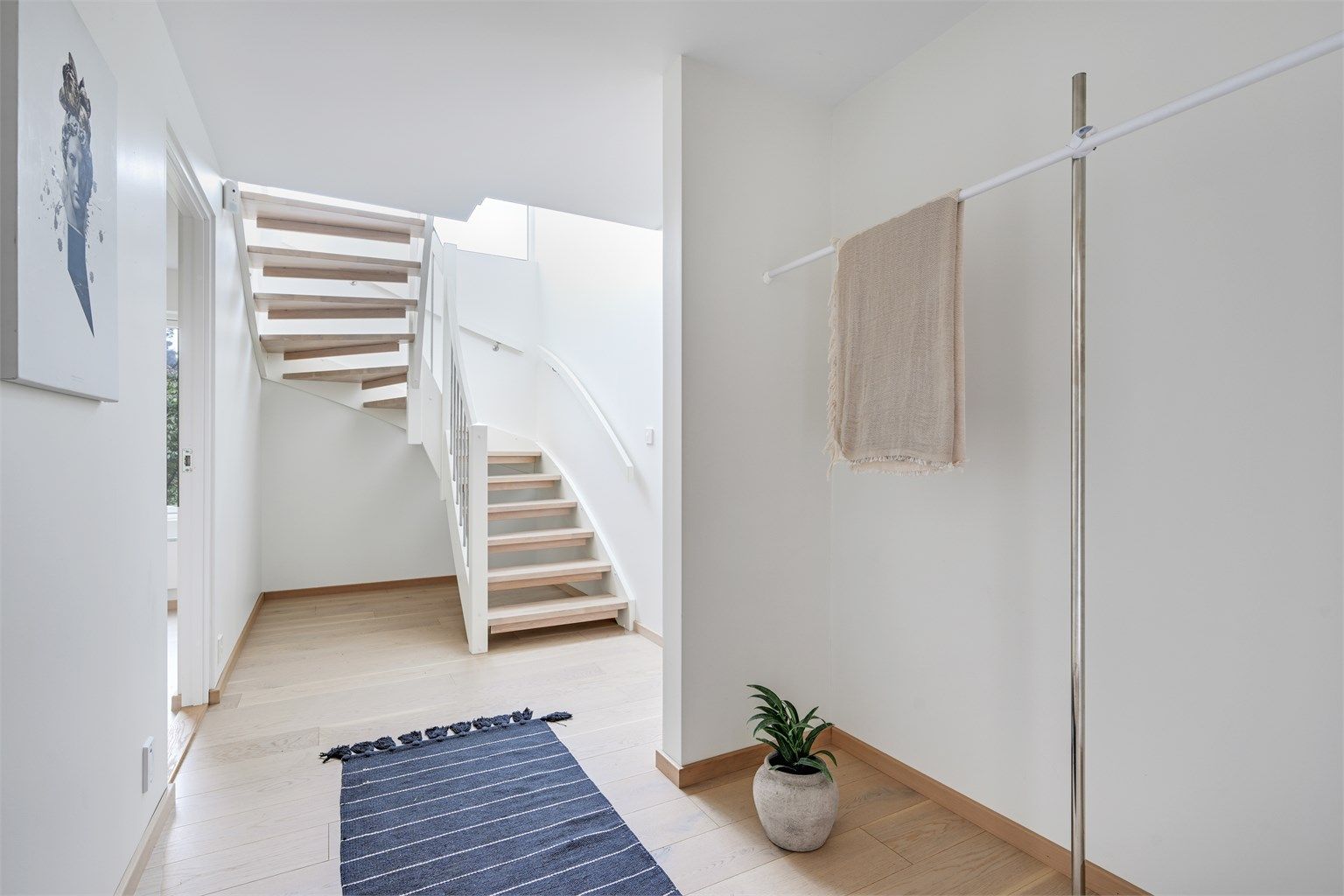 Hallen ønsker velkommen med parkett på gulvet og en malt tretrapp med eiketrinn som binder etasjene sammen.