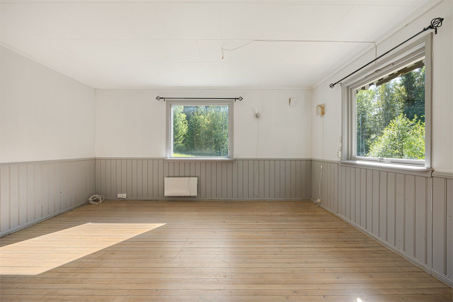 Rommet har panel på deler av veggene og vinduer som vender ut mot hagen.