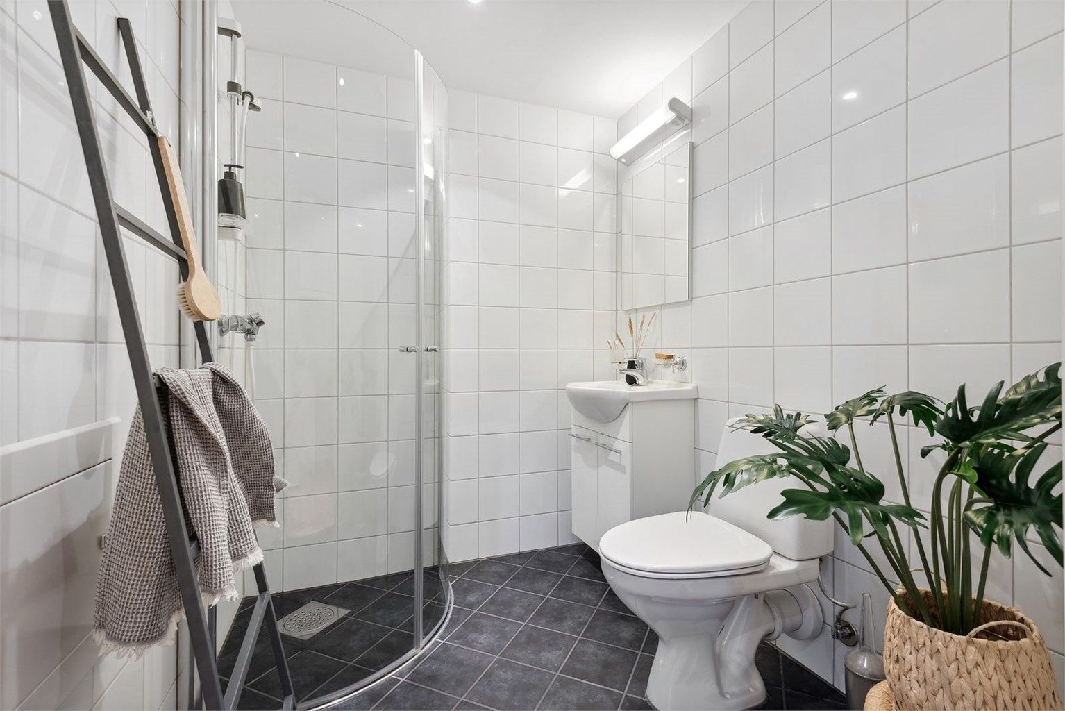 Badets areal er like velutnyttet som i resten av leiligheten. Dusjhjørnets buede glassdører kan svinges inn. I hjørnet innenfor døren er det plass til vaskemaskin.