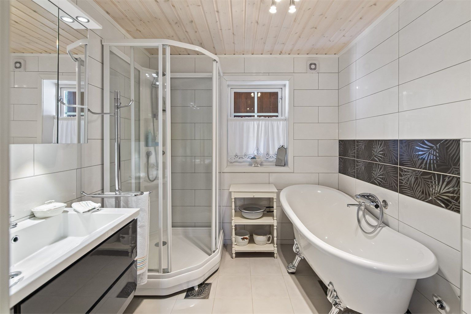 Badet er innredet med badekar, dusjkabinett, vegghengt toalett og servant i innredning